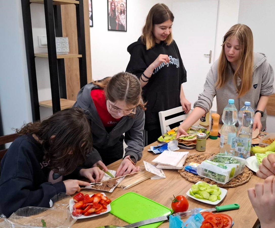 zdjęcie: dziewczęta przygotowują zdrowe przekąski, na stole kuchennym widać różne produkty