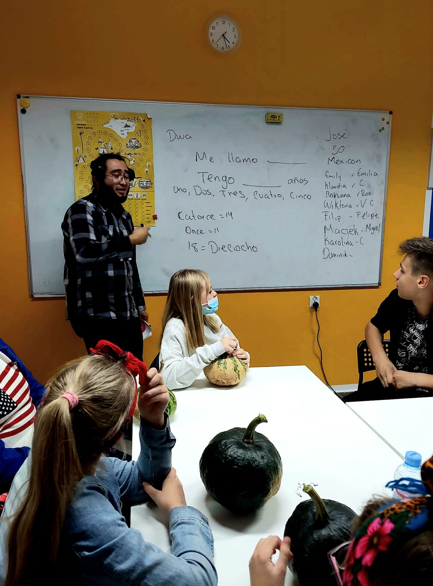 zdjęcie: dzieci siedzą przy stole, przy tablicy stoi mężczyzna z flamastrem w ręce